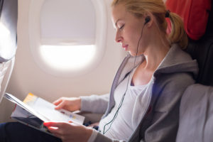 Uma mulher lendo uma revista e ouvindo música no avião. Mulher viajante lendo sentada na cabine de passageiros. O sol brilhando através da janela do avião.