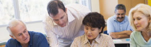 Adult students in class drawing pictures with teacher helping (selective focus)