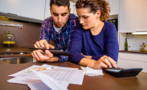 Serious young couple reviewing their bank accounts with a digital tablet and calculator at home. Financial family concept. ** Note: Soft Focus at 100%, best at smaller sizes